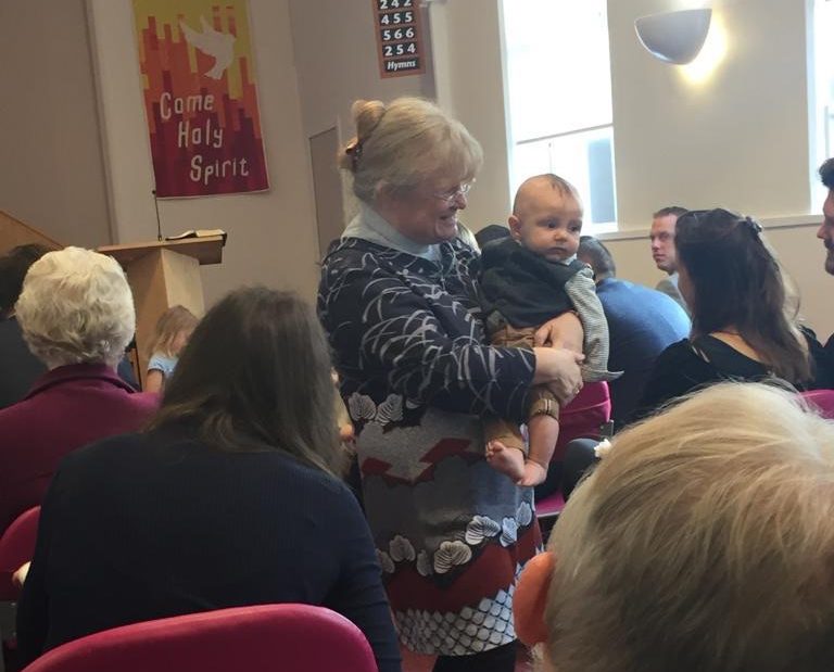 A baby being carried through the congregation at a baptism